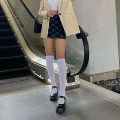 Person in a plaid skirt, blazer, and knee high socks on an escalator