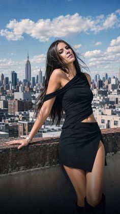 Woman in a black top and mini skirt posing on a rooftop with a cityscape background