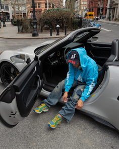 Person in a blue hoodie and ripped jeans sitting in a silver convertible car