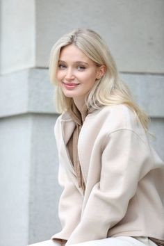 Blonde woman in a beige jacket and hoodie smiling outdoors