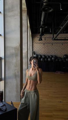 Woman in a sports bra and sweatpants taking a mirror selfie in a gym