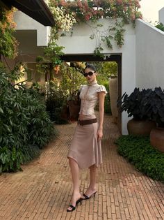 Woman in a beige top and midi skirt with sunglasses on a garden path