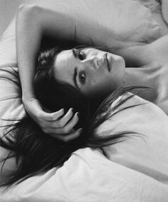 Woman with long hair lying in bed, looking up at the camera