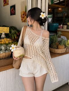 Woman in a crochet top and bikini at a fruit stand, holding a coconut