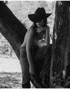 Woman in a cowboy hat and jeans posing on a tree branch