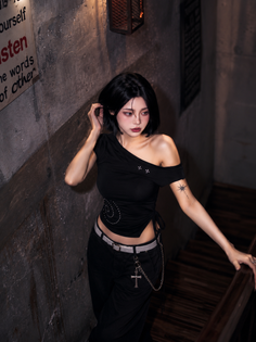 Woman with short black hair in a dark top and pants in a dimly lit indoor setting