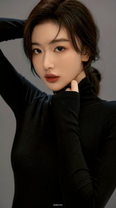 Woman in a black turtleneck with hands behind her head, looking at the camera