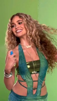 Woman with curly hair in a green crop top and jewelry against a green background