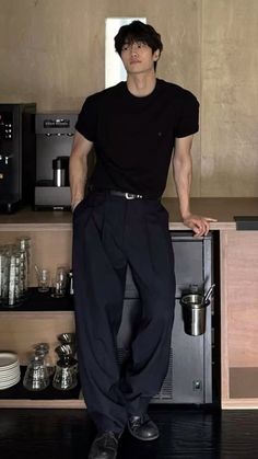 Man in a black t-shirt and dark pants leaning on a counter in a coffee shop