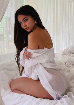 Woman with long dark hair in a white shirt on a bed
