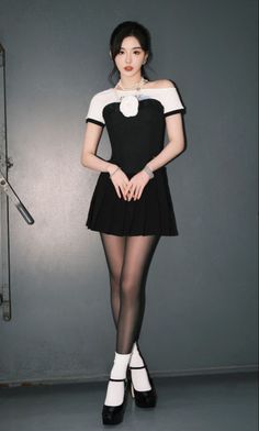 Woman in a black dress with a pleated skirt and pearl necklace standing indoors
