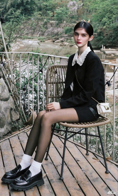 Woman with black hair and a white lace collar sitting outdoors by a river