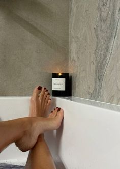 Feet with red nail polish in a bathtub with a lit candle
