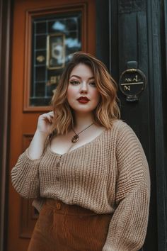 Woman with wavy hair and red lipstick wearing a knitted sweater and corduroy pants