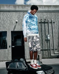 Man in a blue hoodie and camo shorts standing on a car