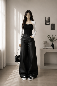 Woman in a black tube top, white bolero, and leather pants standing indoors