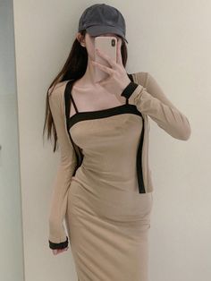 Woman in a beige dress and baseball cap taking a mirror selfie