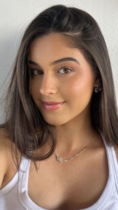 Young woman with long brown hair wearing a white tank top and silver jewelry