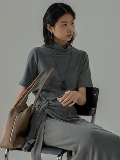 Woman in a gray turtleneck dress with a brown bag, sitting indoors