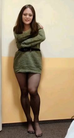 Woman in a green sweater dress and black tights standing indoors