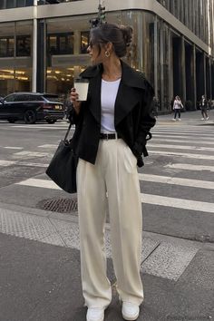Woman in a black jacket and wide leg pants holding a coffee cup on a city street