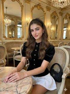 Woman with long brown hair in a black top and white skirt in an ornate cafe