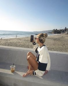 Woman taking a photo of the beach while sitting on a concrete wall