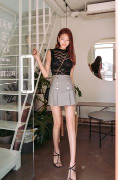 Woman in a sheer black top and grey mini skirt walking indoors