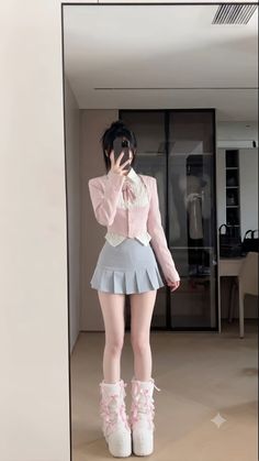Person in a pink jacket and pleated skirt taking a mirror selfie