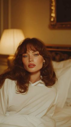 Woman with red hair and freckles in a white shirt in a warm-toned bedroom