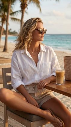 Woman with blonde hair and sunglasses sitting at a table on a beach