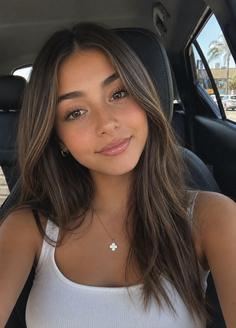 Woman with long brown hair and freckles wearing a white tank top in a car