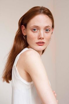 Woman with red hair and freckles wearing a white top and nose ring