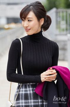 Woman in a black turtleneck and plaid skirt holding a magenta coat outdoors