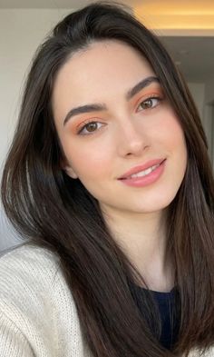 Woman with long brown hair and orange eyeshadow wearing a white sweater