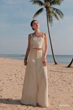 Woman in a crochet two-piece outfit on a sandy beach with a palm tree