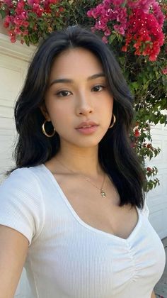 Woman with black hair wearing a white top and gold jewelry outdoors