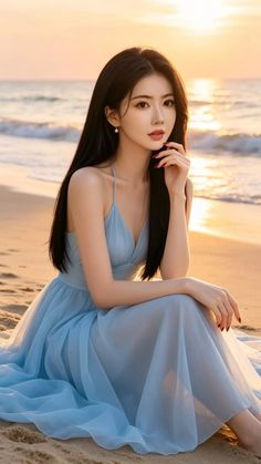 Woman in a blue dress sitting on a beach at sunset