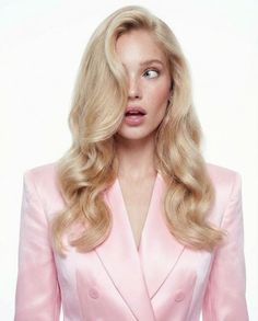 Woman with blonde hair and freckles wearing a pink blazer against a white background