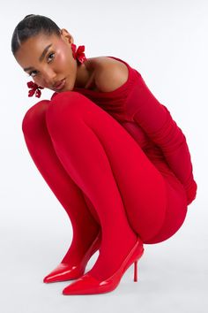 Woman in a red outfit, tights, and heels squatting in a studio