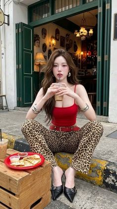 Woman in leopard print pants and a red crop top sitting on a curb