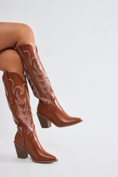 Person wearing brown cowboy boots with white embroidery on a white background