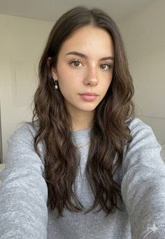 Woman with long wavy hair and freckles wearing a grey sweatshirt and pearl earring