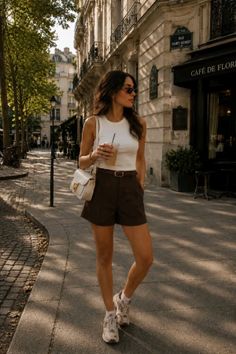 Woman in a white tank top and brown shorts walking on a street during the day