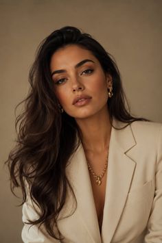 Woman with long dark hair wearing a beige blazer and gold jewelry