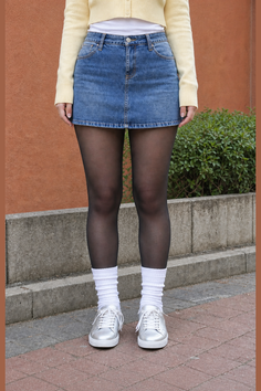 Person wearing a denim skirt, black tights, and silver sneakers outdoors