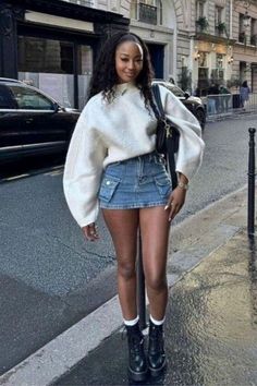 Woman in a white sweater and denim skirt standing on a wet street