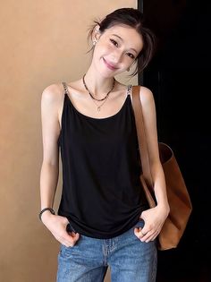 Woman in a black tank top and blue jeans with a brown bag and layered necklaces