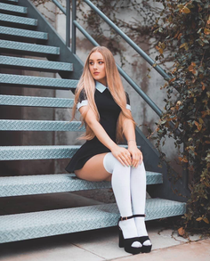 Woman with long blonde hair in a black dress and white knee socks sitting on metal stairs