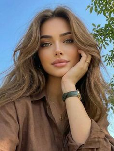 Woman with long brown hair and green eyes wearing a brown shirt outdoors
